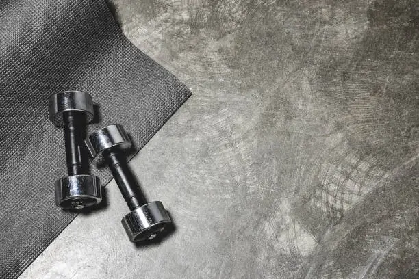 Photo of top view of yoga mat and dumbbells lying on concrete surface