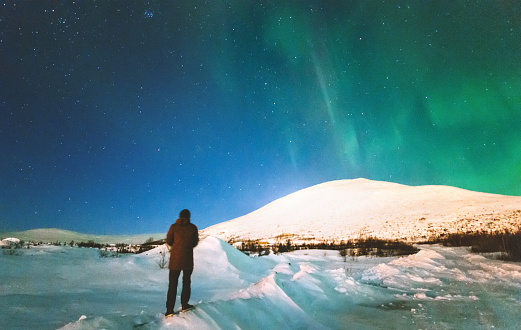 Traveler man enjoying Northern lights view above mountains Travel Lifestyle emotional concept vacations into the wild night scene