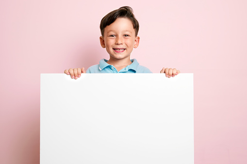 Portrait of a cute child holding white poster isolated on pink background for your text message.