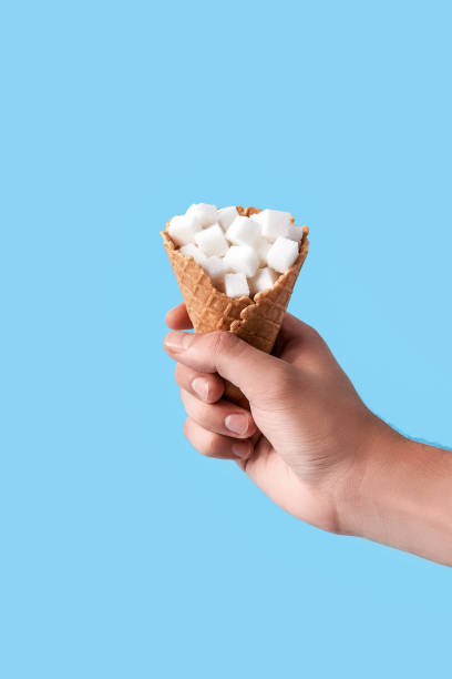 man holding in hand ice-cream wafer cone filled with white sugar cubes isolated on blue background stock photo