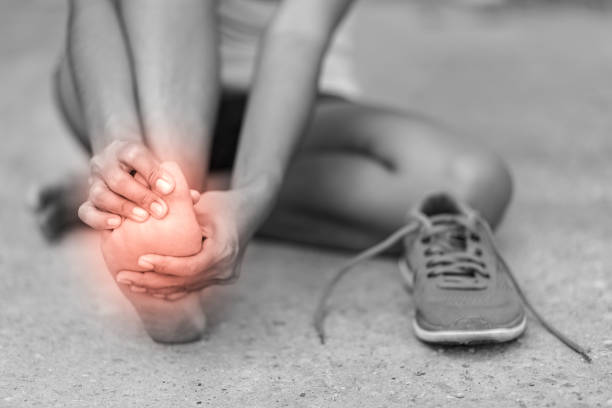 joven dando masajes a su pie doloroso de hacer ejercicio y correr, foto blanco y negro con punto rojo. - sport massaging accident adult fotografías e imágenes de stock