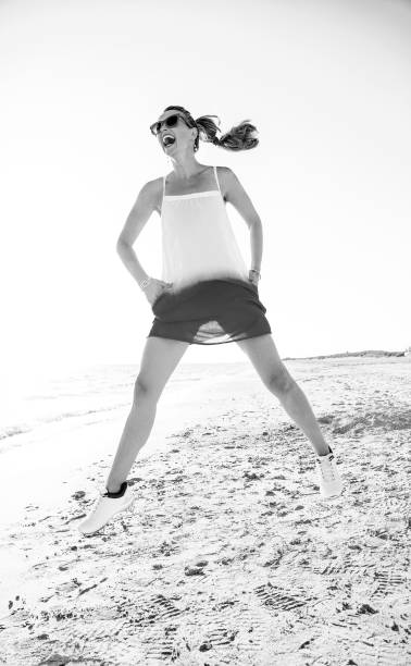 istock smiling modern woman on seashore in evening jumping 1032681838