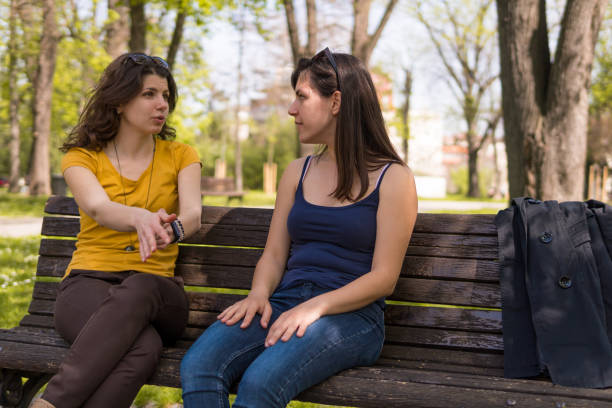istock Two caucasian girls sitting on a park bench and talking 1032716946