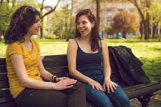 istock Two caucasian girls sitting on a park bench and talking 1032717666