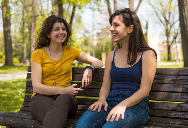 istock Two caucasian girls sitting on a park bench and talking 1032720130