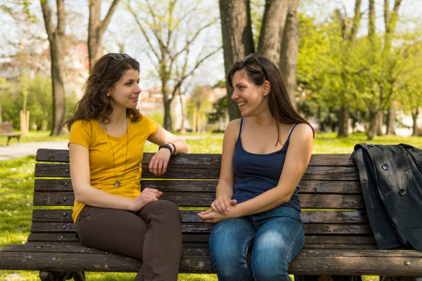 istock Two caucasian girls sitting on a park bench and talking 1032720678