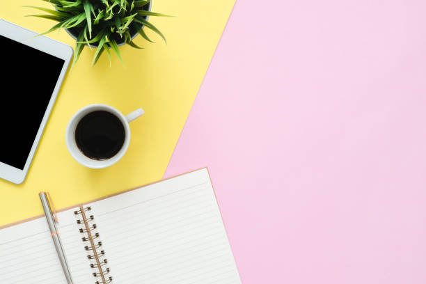 istock Office desk working space - Flat lay top view photo of working space with blank mock up tablet, coffee cup and notebook on pastel background. Pastel pink yellow color copy space working desk concept. 1032720690