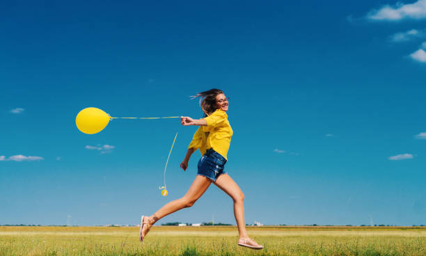 Cheerful young girl in yellow shirt running in field with yellow balloon in her hand. Cheerful young girl in yellow shirt running in field with yellow balloon in her hand. free of charge photos stock pictures, royalty-free photos & images