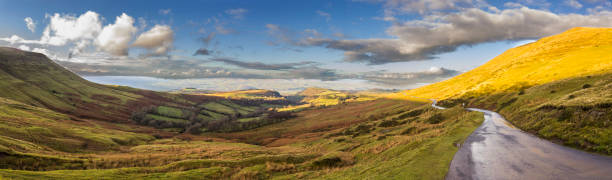 A panoramic view from Gospel Pass at Black Mountains during sunset with incredible views of Wales countryside, grass, road, meadows and hills illuminated by the last lights from the sun. Wales, UK