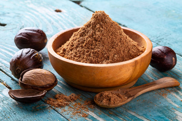 tuerca entera con cáscara, agrietado y nuez moscado en polvo en un cuenco de madera y cuchara en viejo fondo rústico azul - nutmeg india spice nut fotografías e imágenes de stock