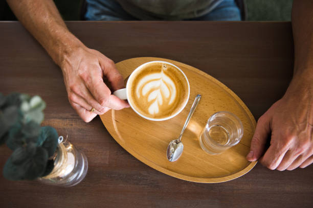 un homme tenant la tasse de café cappuccino et un verre d’eau sur un plateau en bois. découvre d’en haut - latte machiatto photos et images de collection