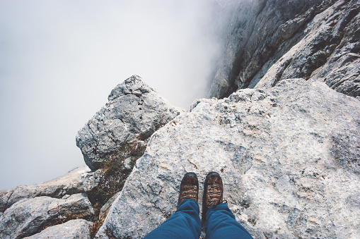 Traveler Feet boots on rocky mountain cliff over foggy clouds Travel Lifestyle success concept adventure active vacations outdoor top view