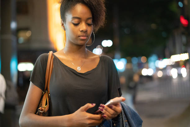 istock Young black woman using mobile in the city at night 1032775874