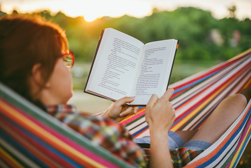 view on teenage girl reading book in hammock in the garden in summer