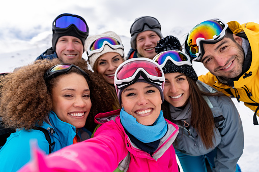 Happy group of people taking a selfie while skiing in the Alps and looking at the camera smiling - winter lifestyle concepts