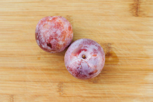 Two honey punch pluot fruits sit on a wooden chopping board