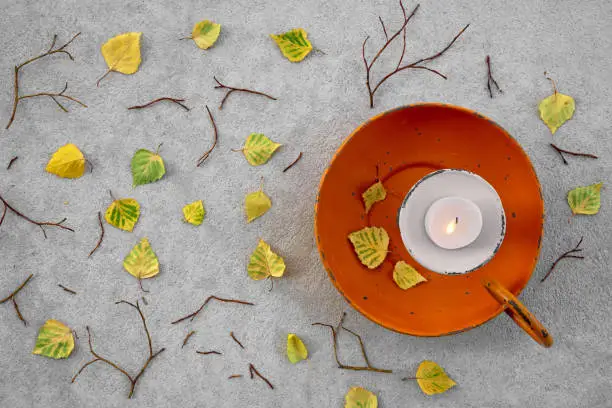 Autumn leaves and cozy candlelight on gray concrete background.