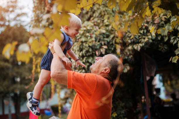 miłość od pierwszego wejrzenia. dumny dziadek bawi się wnukiem na podwórku, podnosząc go w powietrzu. - grandfather baby grandson grandparent zdjęcia i obrazy z banku zdjęć