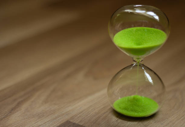 istock Hourglass with green sand on a wooden background 1032834496