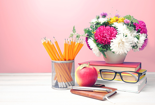 Teachers day,flowers pencils stack of books and apple on table empty space background.