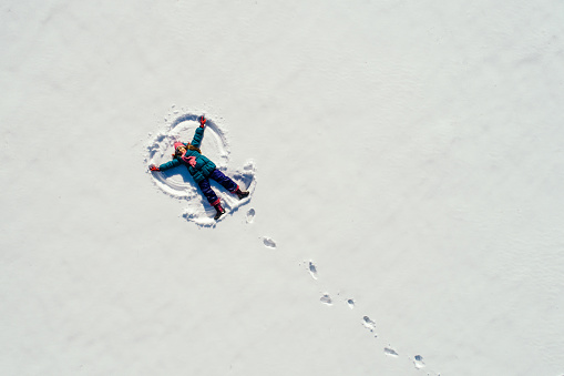 Little girl lying on the snow at sunny day and making snow angel. Photo taken with drone directly above