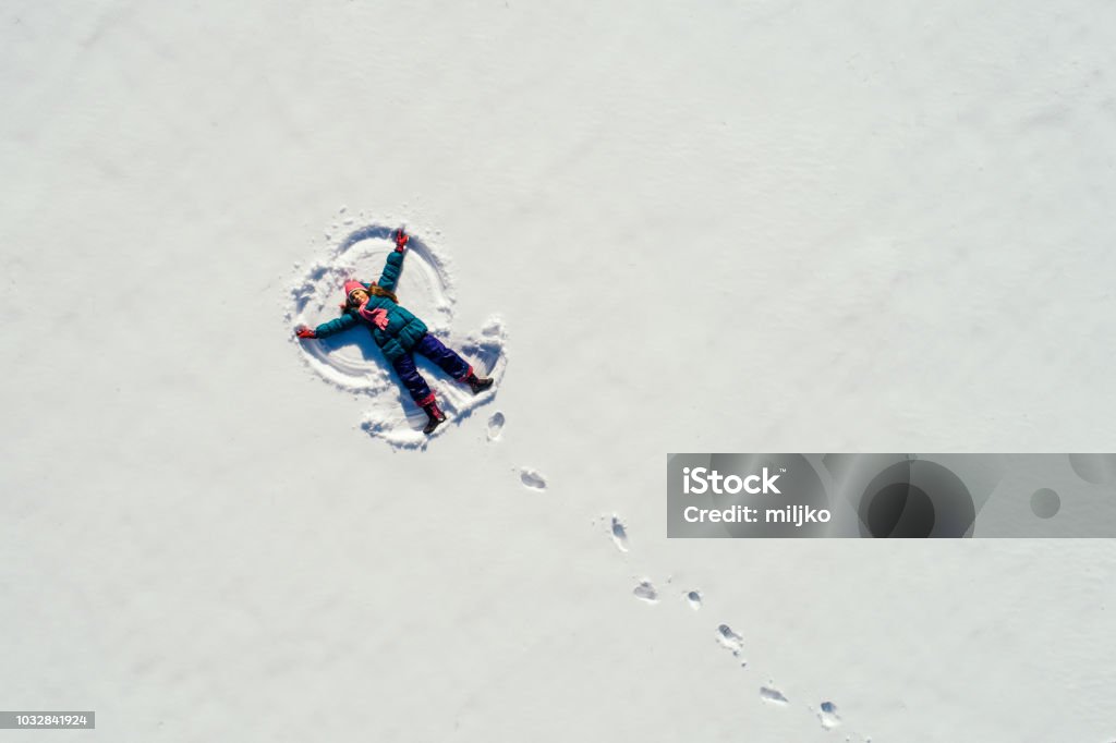 Girl making snow angel Little girl lying on the snow at sunny day and making snow angel. Photo taken with drone directly above Snow Stock Photo