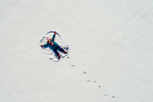 Girl making snow angel Little girl lying on the snow at sunny day and making snow angel. Photo taken with drone directly above snow angels stock pictures, royalty-free photos & images