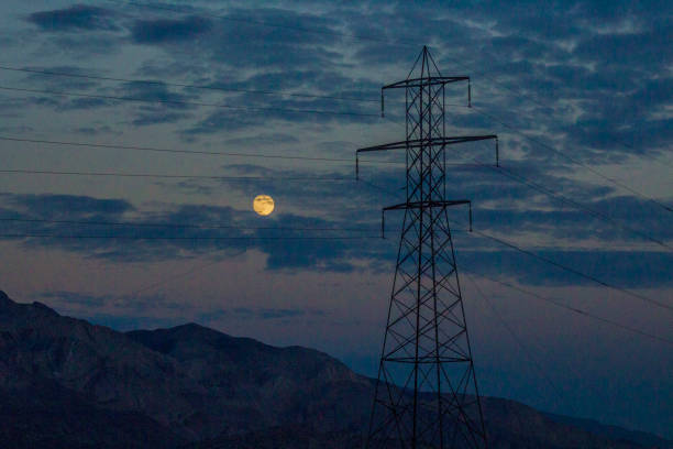 An orange moon hangs in the dusk over a telephone pole in the desert outside of Lone Pine, CA near Death Valley.