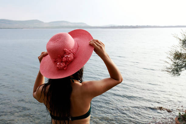 Young woman in hat standing on beach. rear view