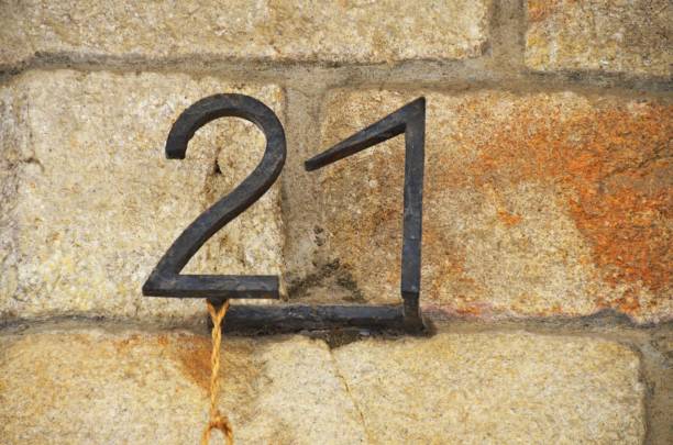 house number 21 on rustic sandstone brick wall, rusty wrought iron metal numbers