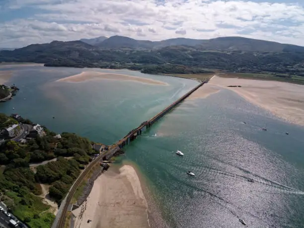 Aerial view, Drone panorama over rising tide sea, bay, anchored boats, steel railway bridge in Barmouth, Wales