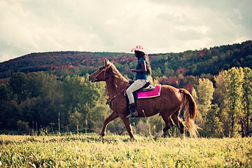 Haitian cowgirl horse rider behind a spectacular autumn landscape. It is a western riding. SHe wear a cowboy hat. Color and horizontal photo was taken in Quebec Canada.