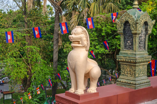 A lion statue or leogryph at the steps of the main stupa  of Wat Phnom (Mountain Pagoda), in Phnom Penh in Cambodia Phnom Penh, Cambodia - April 8, 2018: A guardian lion statue or leogryph in front of the main stupa of Wat Phnom (Mountain Pagoda) and a garden decorated with national and Buddhist flags for the celebration of the Cambodian New Year khmer stock pictures, royalty-free photos & images