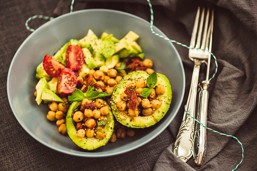 Superfood Salad with Avocado, Chickpeas and Dried Tomato decorated with mint leaves and grains of mustard seed