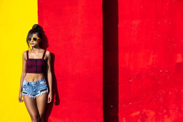 Beautiful woman with sunglasses standing in front of colored background.