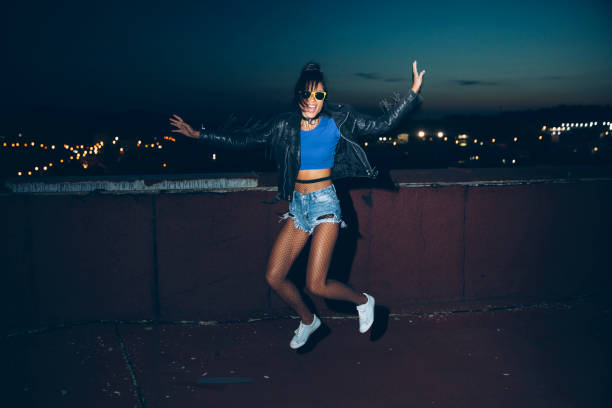 Young Woman Midair Jump Against Blue, Wearing Black Top And Jeans, Airborne Pose, Dynamic Expression, Motion