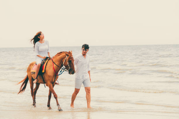 istock Young couple goes horse riding on tropical beach. 1032940984