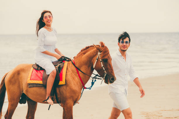 istock Young couple goes horse riding on tropical beach. 1032940986