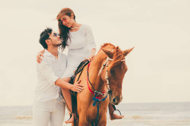 istock Young couple goes horse riding on tropical beach. 1032941008