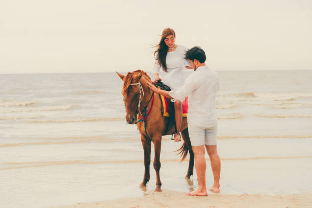 istock Young couple goes horse riding on tropical beach. 1032941010