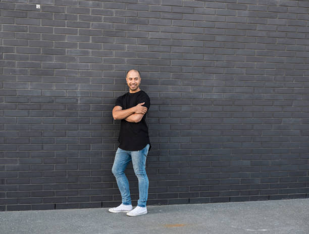 ritratto di sorridente uomo di razza mista maori/caucasico in jeans casual e abiti da maglietta contro un muro di mattoni neri in nuova zelanda, nuova zelanda - minority white simplicity confidence foto e immagini stock