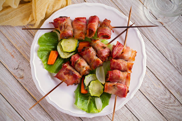 Chicken liver wrapped with bacon on skewers. Grilled liver kebabs Chicken liver wrapped with bacon on skewers. Grilled liver kebabs with vegetables on white plate. overhead, horizontal chicken skewer stock pictures, royalty-free photos & images