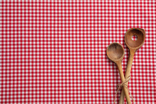 Wooden kitchen utensils on red and white checkered picnic tablecloth, top view, copy space