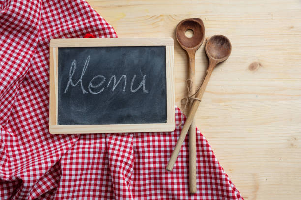 Menu concept. Blackboard and kitchen utensils on red tablecloth, wooden table, space for text, top view