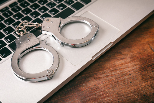 Cybercrime concept. Handcuffs on a computer on a wooden background, copy space.