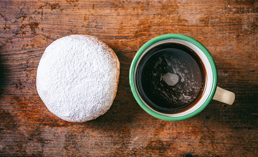 Breakfast concept. Coffee and krapfen with powder sugar, two, with top view and isolated on wooden background.