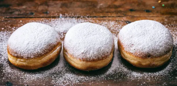 Jelly filled doughnuts concept. Krapfen with powder sugar, three and isolated on wooden background.
