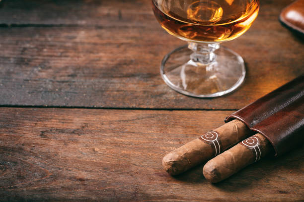 flou de cigares cubains agrandi sur le bureau en bois, verre de brandy - cigar whisky bar cognac photos et images de collection