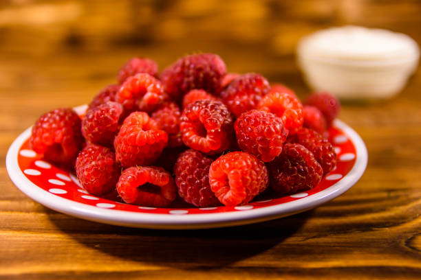 istock Ceramic plate with ripe raspberries and sour cream on wooden table 1033037480