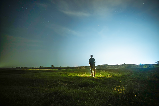 one man standing in the grass field under sky at night